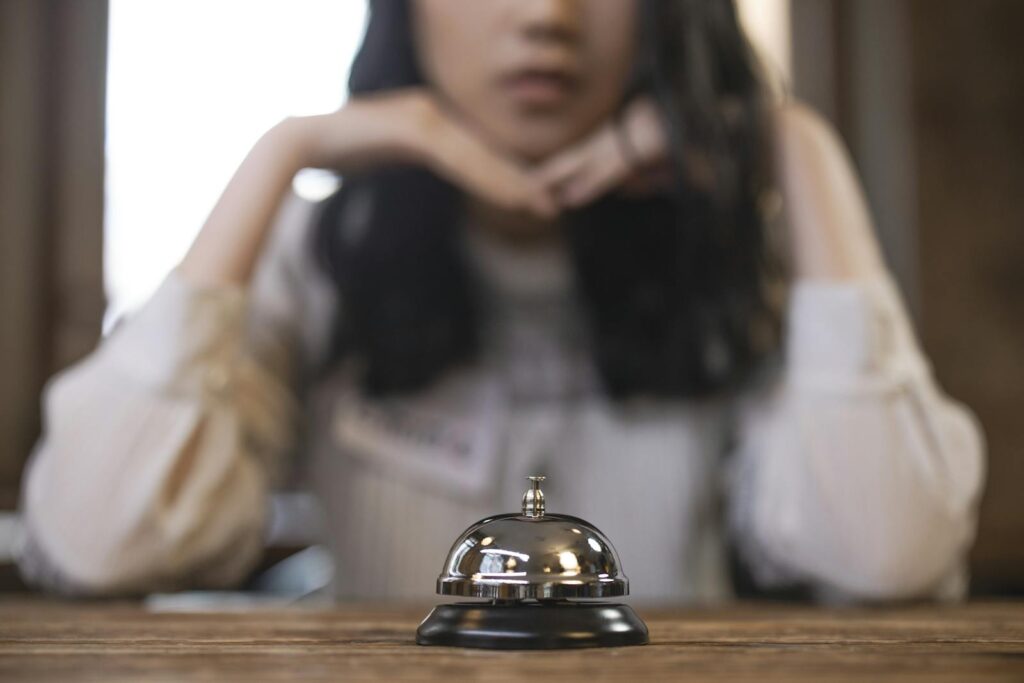 Reception bell on a wooden table with a blurred person in the background, creating focus on hospitality service.
